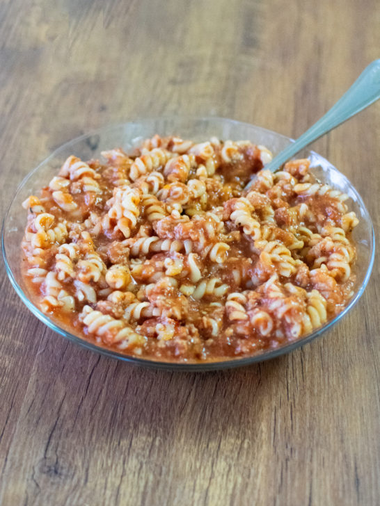 Very Easy American Goulash in a clear bowl with a fork on a dark wood table.