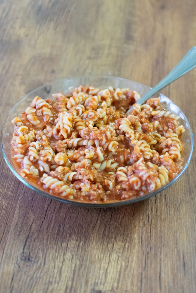 Easy American Goulash in a clear bowl with a fork on a dark wood table.