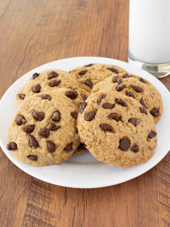 Easy Chocolate Chip Oatmeal Cookies on a white plate on a dark wood background with a clear glass of milk nearby