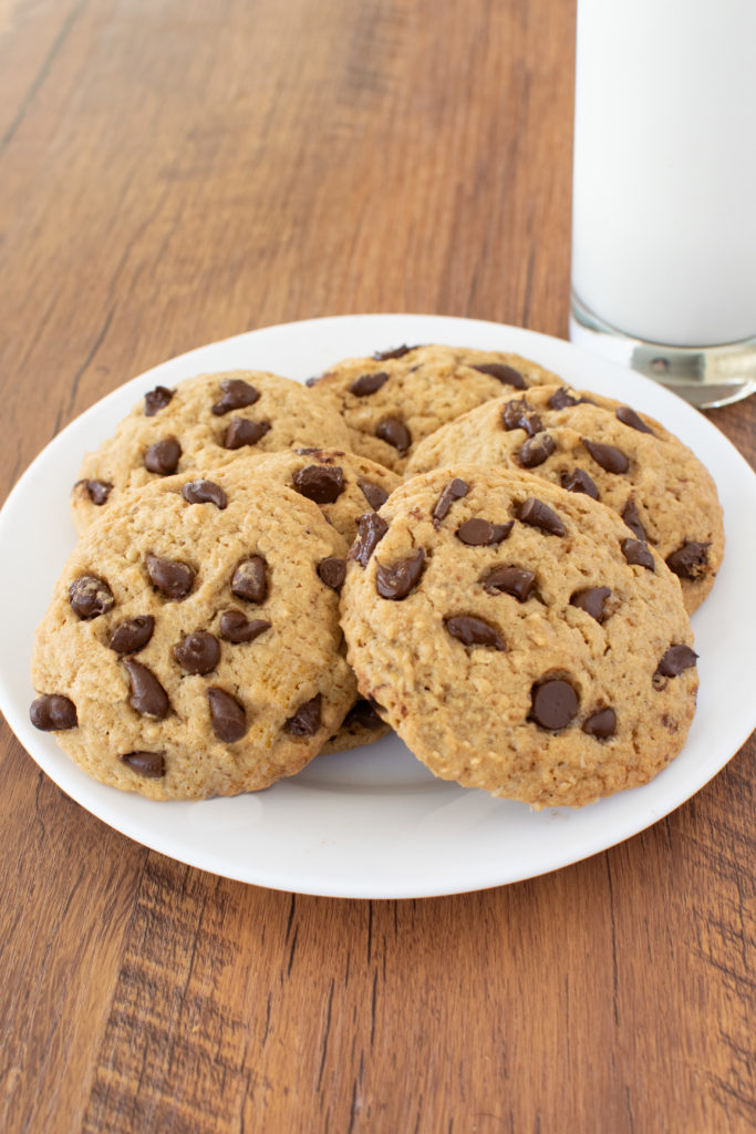 Easy Chocolate Chip Oatmeal Cookies on a white plate on a dark wood background with a clear glass of milk nearby 