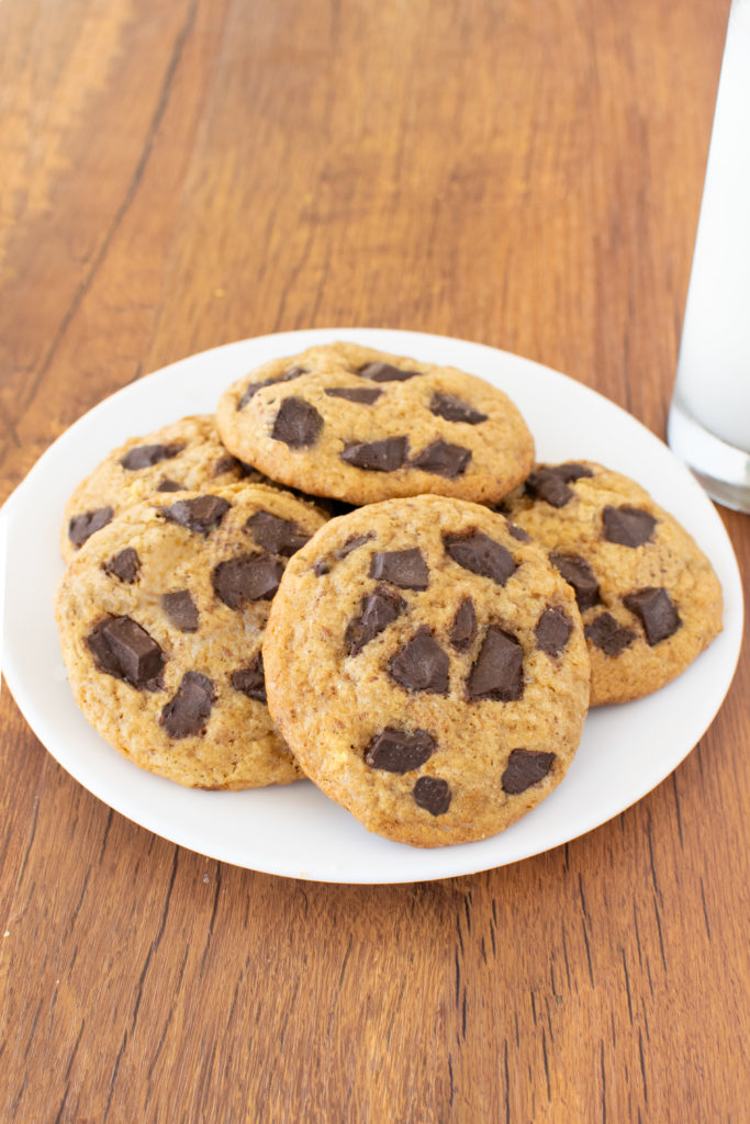 Easy Cakey Chocolate Chunk Cookies on a white plate with a clear glass of milk nearby on a dark wood table.