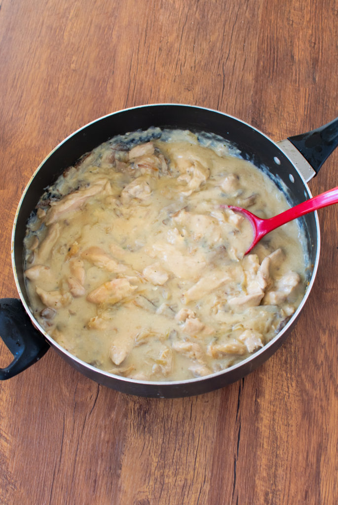 Easy dairy-free chicken stroganoff in a pan with a red serving spoon on a dark wood table