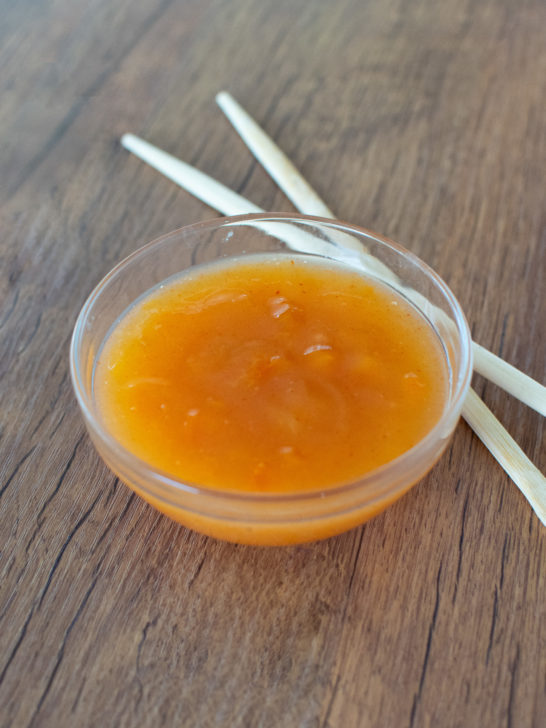 Easy homemade duck sauce in a glass bowl on a dark brown table with chopsticks nearby.