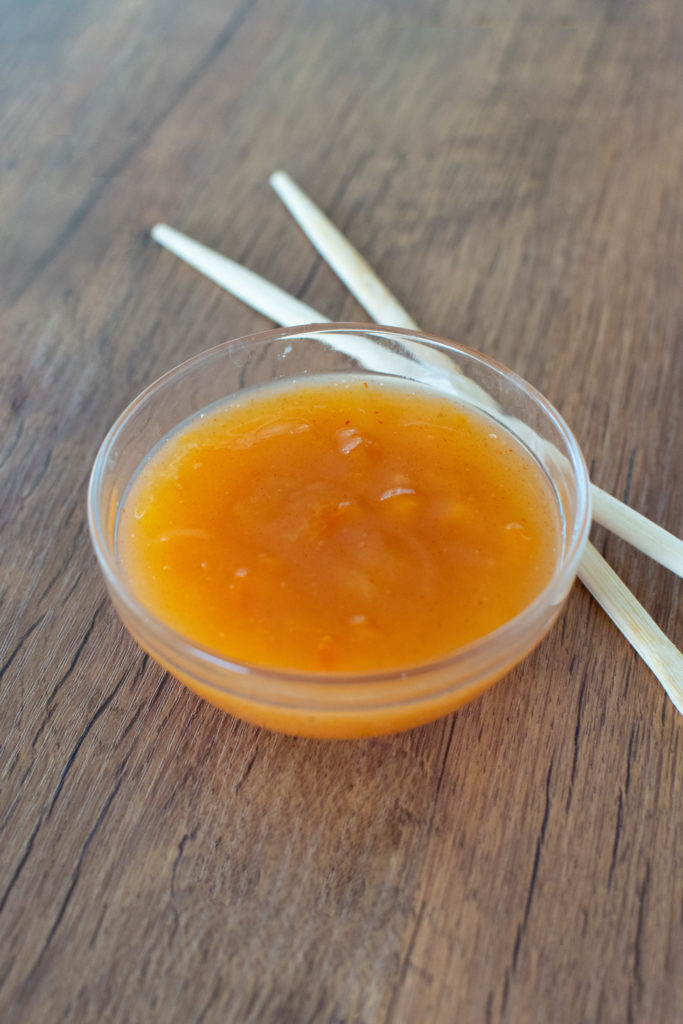 Easy homemade duck sauce in a glass bowl on a dark brown table with chopsticks nearby.