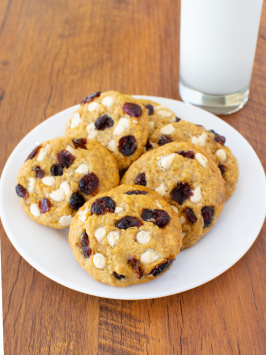 Easy Oatmeal Cranberry White Chocolate Cookies on a white plate with a clear glass of milk nearby on a dark wood table.