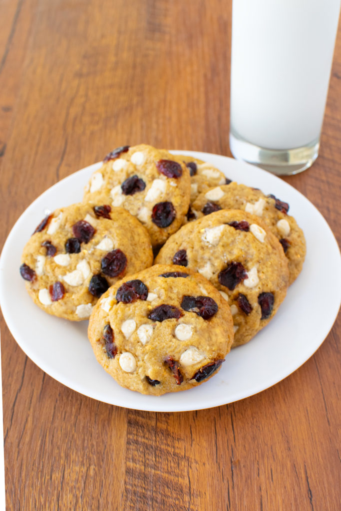 Easy Oatmeal Carnberry White Chocolate Cookies on a white plate with a clear glass of milk nearby on a dark wood table.