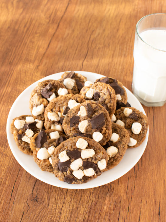 Easy S'more Cookies on a white plate near a clear glass of milk on a dark wood table.