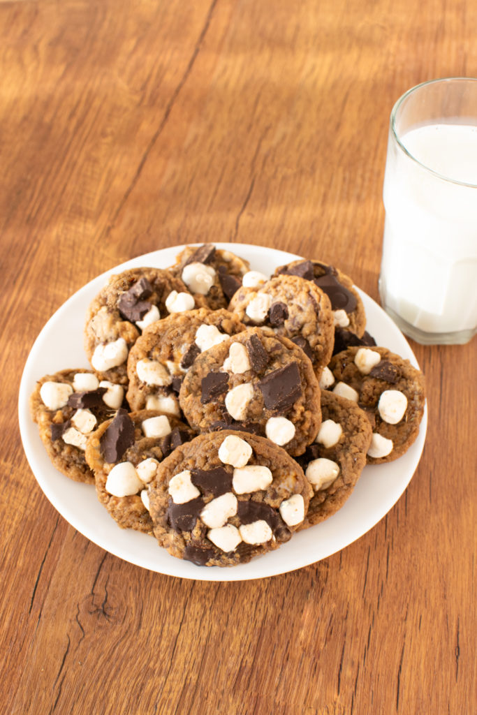 Easy S'more Cookies on a white plate near a clear glass of milk on a dark wood table.