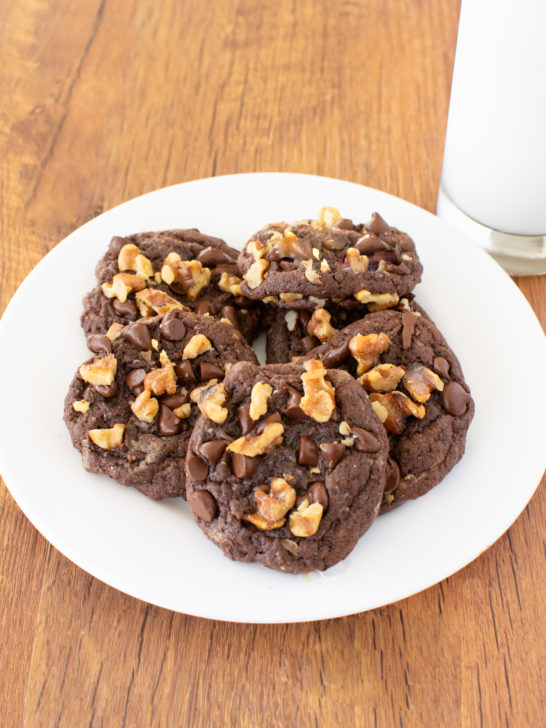 Easy Chocolate Chocolate Chip Walnut Cookies on a white plate by a clear glass of milk on a dark wood table