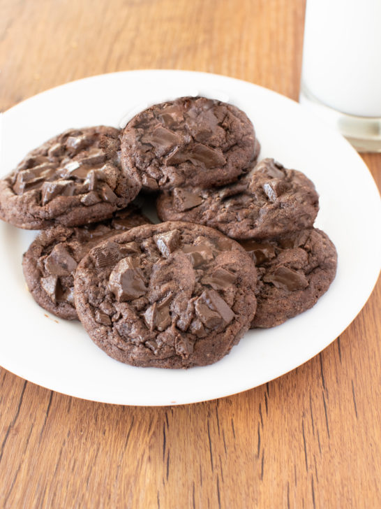 Easy Chocolate Chocolate Chunk Cookes on a white plate near a clear glass of milk on a dark wood table