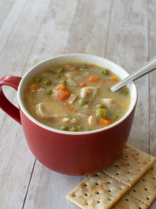 Easy Dairy-Free Chicken Pot Pie Soup in a red soup mug with a spoon near saltine crackers on a white wood table